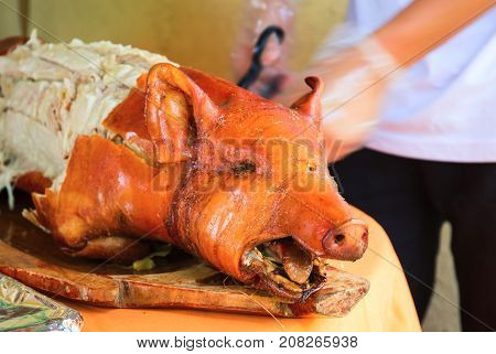 Fried pork on table. Waiter cut whole pork. Traditional dish whole roasted pig with head. Delicious meat barbecue. Roasted pork for serving. Fresh juicy pork meat for lunch. Philippines lechon