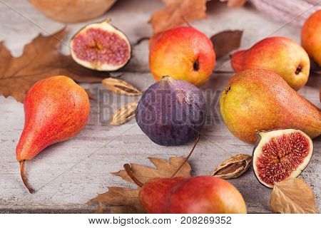 Abstract composition of fresh ripe organic pears figs and dry leaves on a white wooden background. Pattern of fruits and leaves. Food background. Autumn harvest concept.