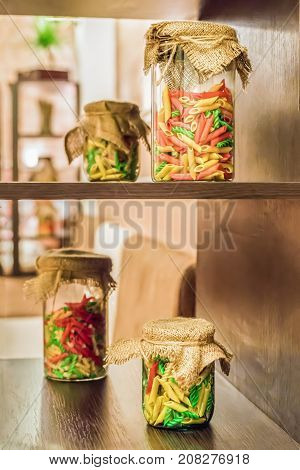 Dry colored pasta in a glass jars on the wooden shelves indoor