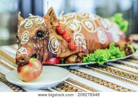 Cooked suckling pig with an apple in his mouth on a white plate on banquet table close up