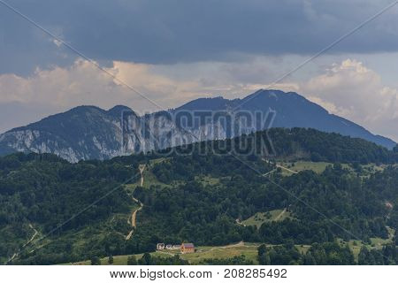 Picturesque rural scenery with house and country road uphill in Carpathian mountain, Romania. Countryside view in Transylvania. Mountains and cloudscape in the background.