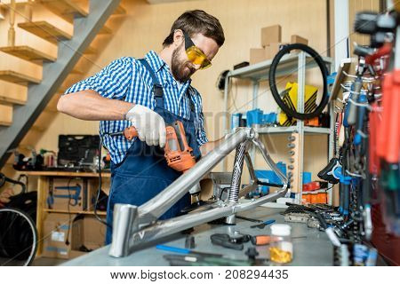 Repairman working with electric drill by workplace in his own workshop