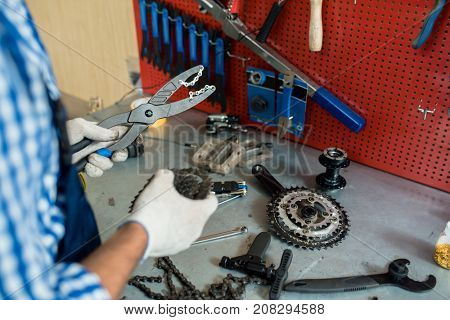 Gloved hands of master holding pliers and chain during bibycle repair
