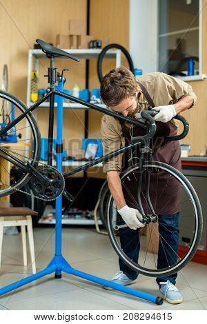 Young master in uniform fixing bolt on wheel of bicycle in workroom