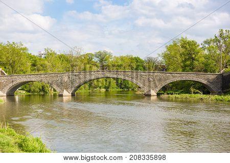solid stone bridge with three arcs over humber river in a natural environment with trees and a cloudy blue sky