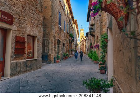 Pienza, Italy - May 27, 2017: Beautiful narrow street with sunlight and flowers in the small magical and old village of Pienza, Val D'Orcia Tuscany.