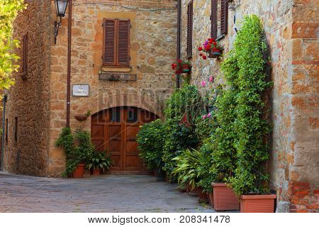 Pienza, Italy - May 27, 2017: Beautiful narrow street with sunlight and flowers in the small magical and old village of Pienza, Val D'Orcia Tuscany.