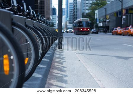 Toronto streetcar in the distance coming down a street with parked taxis and a row of wheels and bikes at a rental station - public transportation
