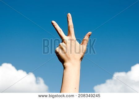 Three finger salute hand gesture on blue sky background