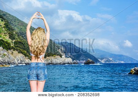 Girl In Monterosso Al Mare Italian Riviera. Curled Hair Woman Showing A Heart Shape. Sea And Mountai