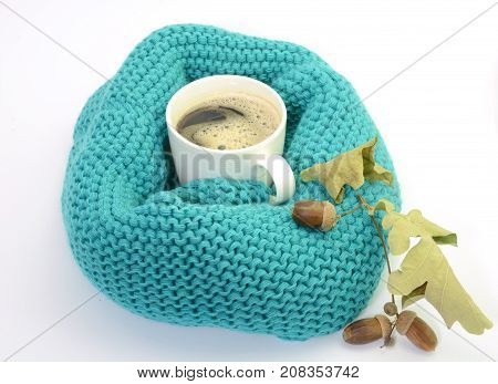 Autumn concept. Knitted turquoise snood scarf, cup of coffee, acorns isolated on white background