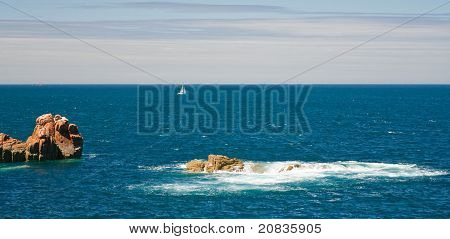 Vista sobre o mar com pedras rosa e iate