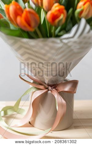 Beautiful orange and yellow tulips on light gray wall. Flower background. Warm colors. copy space. in a vase on a wooden table. bow out of ribbons