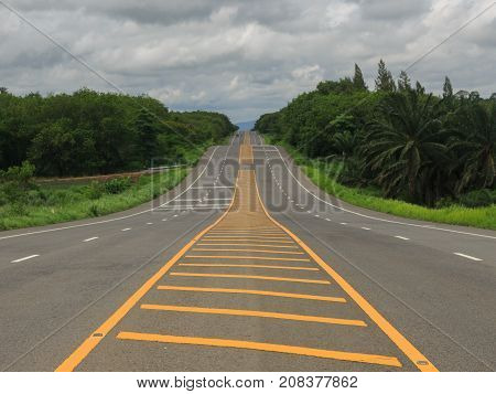 Long hilly road passes through green countryside with cloundy sky.