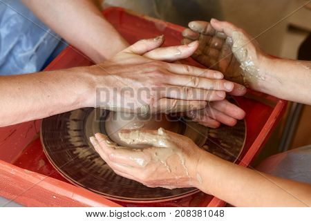 Hands of two people create pot on potter's wheel. Teaching pottery carftman's hands guiding
