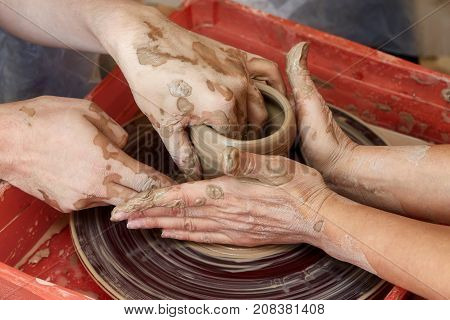 Hands of two people create pot on potter's wheel. Teaching pottery carftman's hands guiding