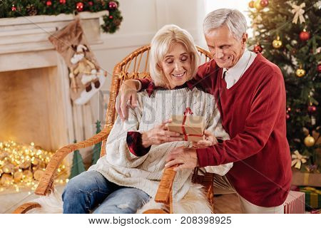 Happy pensioners. Pretty woman keeping smile on her face and bowing head while looking at present