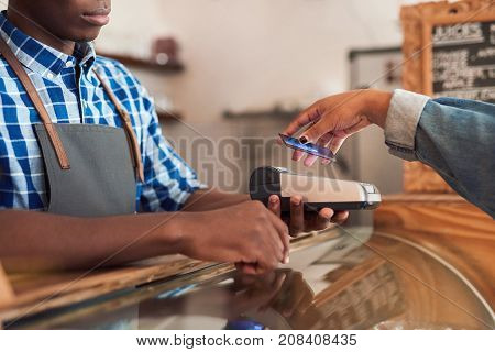 Closeup of a customer using her bank card and nfs technology to pay a barista for her purchase at a cafe