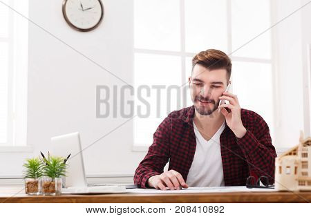 Important call. Young smiling businessman in casual talking on mobile phone in modern white office interior.