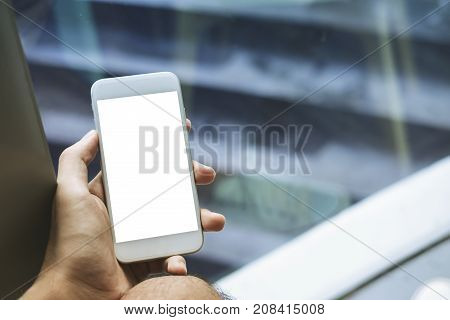 Mockup image of a man's hand holding white mobile phone with blank screen on thigh with white canvas shoes in modern cafe with feeling relax