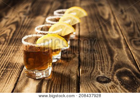 four glasses of whiskey with lemon wooden background