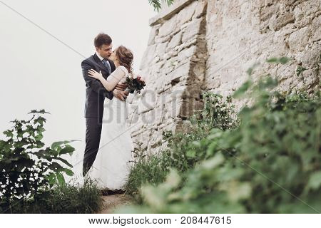 Beautiful Gorgeous Bride And Groom Walking In Sunny Park And Kissing. Happy Wedding Couple Hugging I