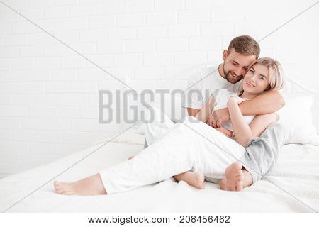 Young loving couple hugging each other, smiling and posing on camera on bed isolated on a white background. Close-up of beautiful couple.