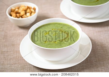 Fresh cream of zucchini soup with olive oil on top served in bowls photographed with natural light (Selective Focus Focus one third into the soup)