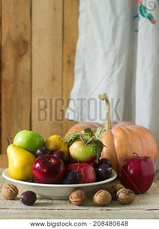 Autumn still life with apples pears plums pumpkin and walnuts on a wooden background. Rustic style selective focus.