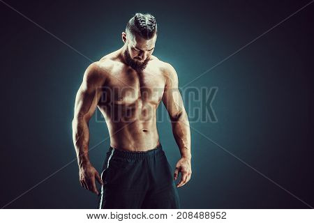 Very brawny guy bodybuilder posing, looking down. Beautiful sporty guy male power. Fitness muscled man in studio. Dark background.