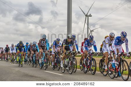 Le Gault-Saint-Denis France - October 08 2017: The peloton riding on a road in the plain with windmills in a cloudy day during the Paris-Tours road-cycling race.