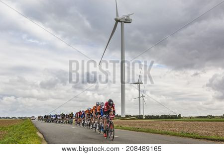 Le Gault-Saint-Denis France - October 08 2017: The peloton riding on a road in the plain with windmills in a cloudy day during the Paris-Tours road-cycling race.