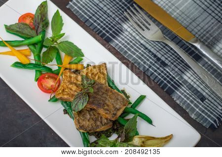 Fried fish with pea pods and cherry tomatoes. Old black background. Top view. Close-up