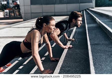 Getting stronger. Young couple in sport clothing doing push-ups while exercising on the stairs outdoors