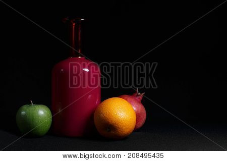 Red bottle orange pomegranate green apple. Still life dark background