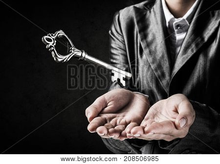 Cropped image of businessman in suit keeping big key in hands with dark wall on background.