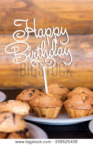Birthday cakes and muffins with wooden greeting sign on rustic background. Wooden sing with letters Happy Birthday and holiday sweets