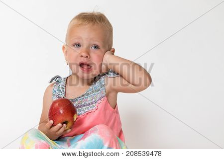 Studio shot of toddler girl holding red apple and touching her aching face