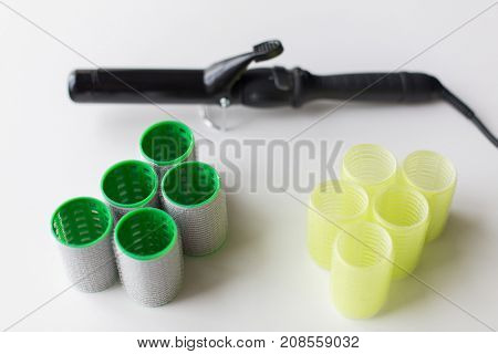 hair tools, beauty and hairdressing concept - curlers or rollers and iron or hot styler on white background
