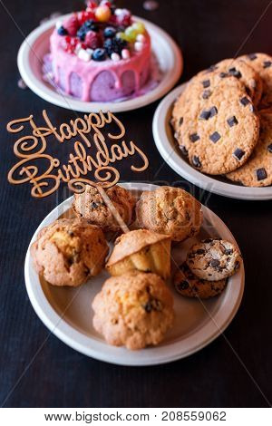 Birthday cake and muffins with wooden greeting sign on rustic background. Wooden sing with letters Happy Birthday and holiday sweets