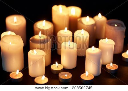 mourning and commemoration concept - candles burning in darkness over black background
