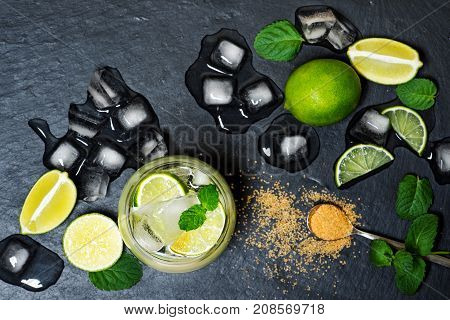 Refreshing mint cocktail mojito with rum and lime, cold drink or beverage with ice on black background, top view