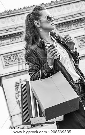 Stylish autumn in Paris. young fashion-monger in trench coat in Paris France with shopping bags having coffee and macaroon