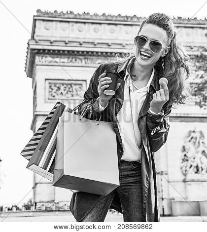 Stylish autumn in Paris. Portrait of smiling young woman in sunglasses with shopping bags near Arc de Triomphe in Paris France having coffee and macaroon