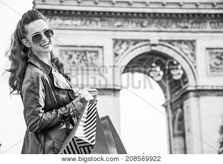 Stylish Christmas in Paris. Portrait of happy young woman in sunglasses with shopping bags and Christmas present near Arc de Triomphe in Paris France