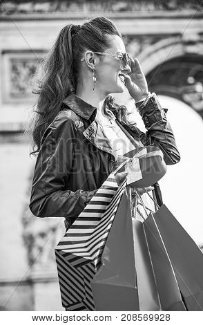 Stylish Christmas in Paris. smiling modern woman in sunglasses with shopping bags and Christmas present near Arc de Triomphe in Paris France looking into the distance