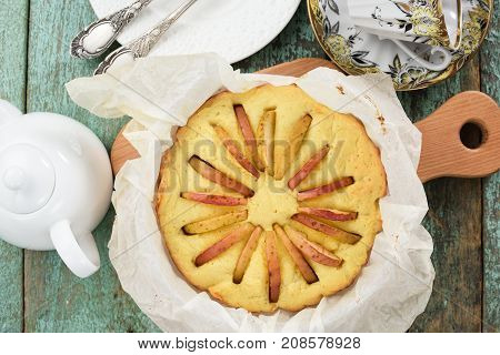 Freshly baked delicious rustic apple cake in baking paper with teaware above view