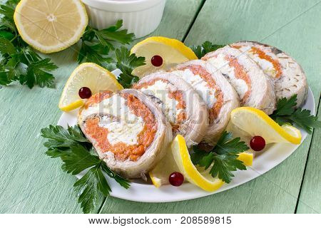 Homemade mackerel roll with carrots and eggs in gelatin. Sliced pieces of rolls are served with lemon cranberries and parsley. Festive snack. Mackerel roll lemon and parsley on green wooden table