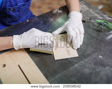 The carved plate on which the patterns and inscriptions are burned out which the master in blue overalls is stripping with a special tool