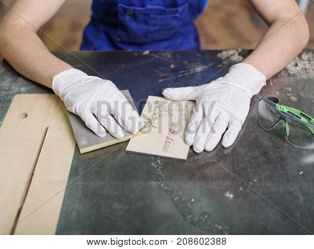 The carved plate on which the patterns and inscriptions are burned out which the master in blue overalls is stripping with a special tool